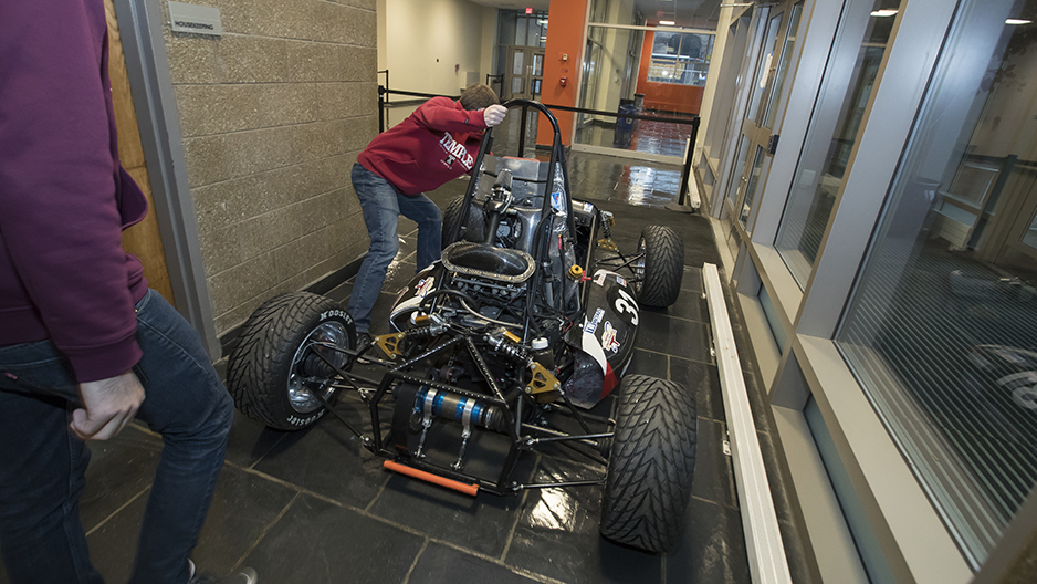 A student pushing the race car through a hallway. 