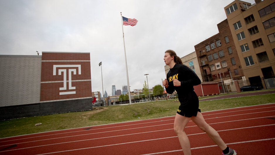 a female ROTC student runs by a building with the Temple 'T'