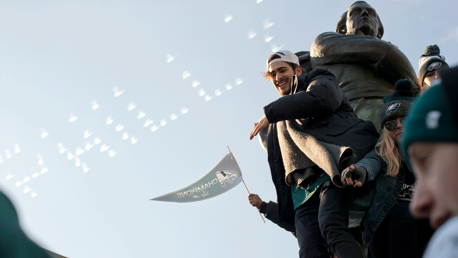 Fans climb statues with "Philly" written in sky behind them