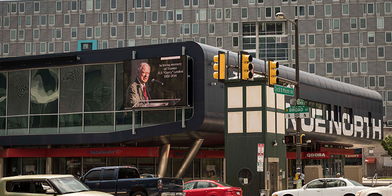 A screen memorializing Gerry Lenfest at a busy intersection in North Philadelphia