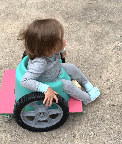 Small child uses fabricated plastic floor wheelchair