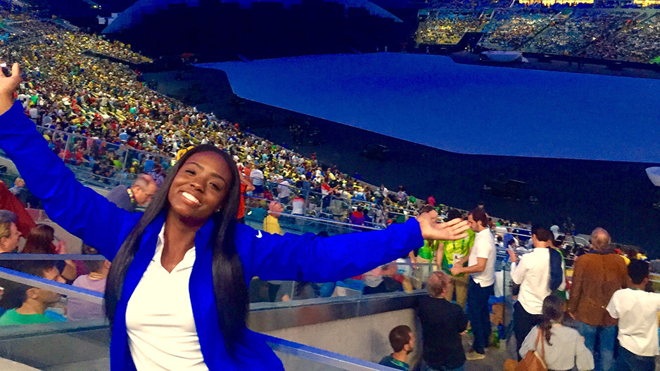 A woman in white shirt and blue jacket smiling at the Summer Olympic Games.