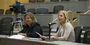 Two women sitting at a table and one is speaking into a microphone.
