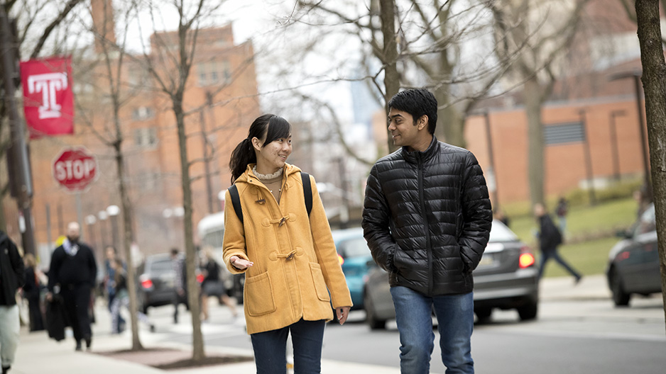 Two students talking to each other as they walk north on 12th Street on campus.