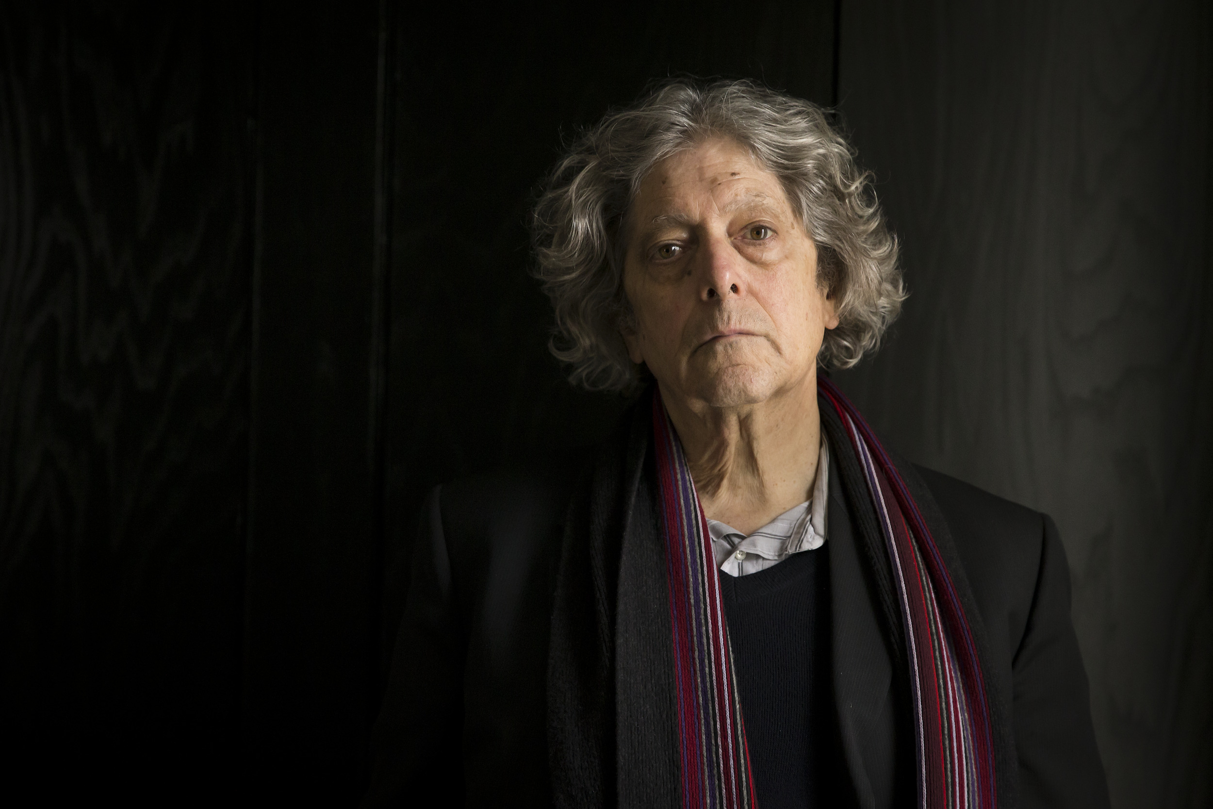 Man with long gray hair wearing a scarf in front of a black background