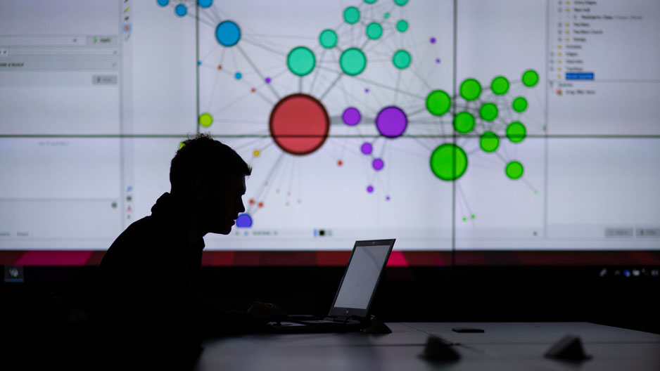 man on a laptop in silhouette with data visualization on screen