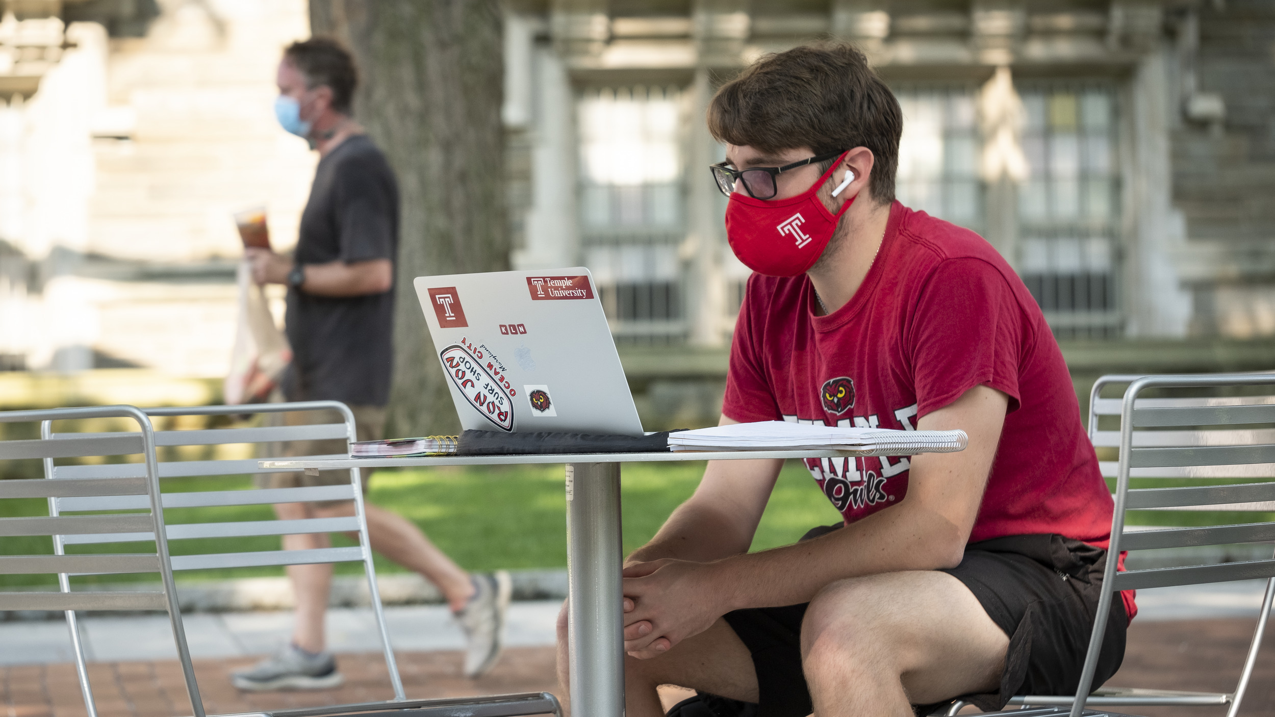 A student sitting outside on campus wearing a mask while using their computer. 