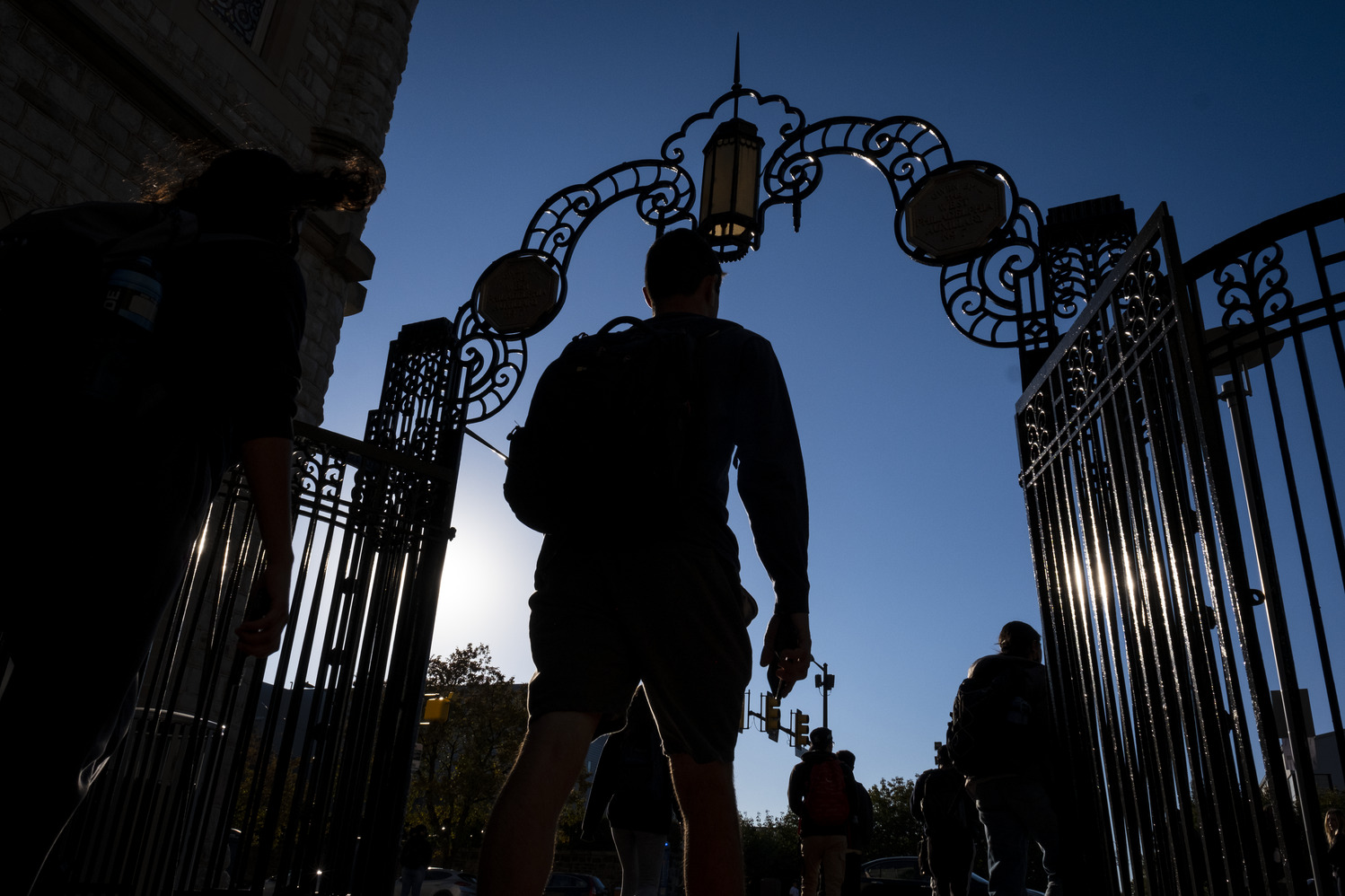 A student in silhouette walks through gates on Temple's Main Campus.