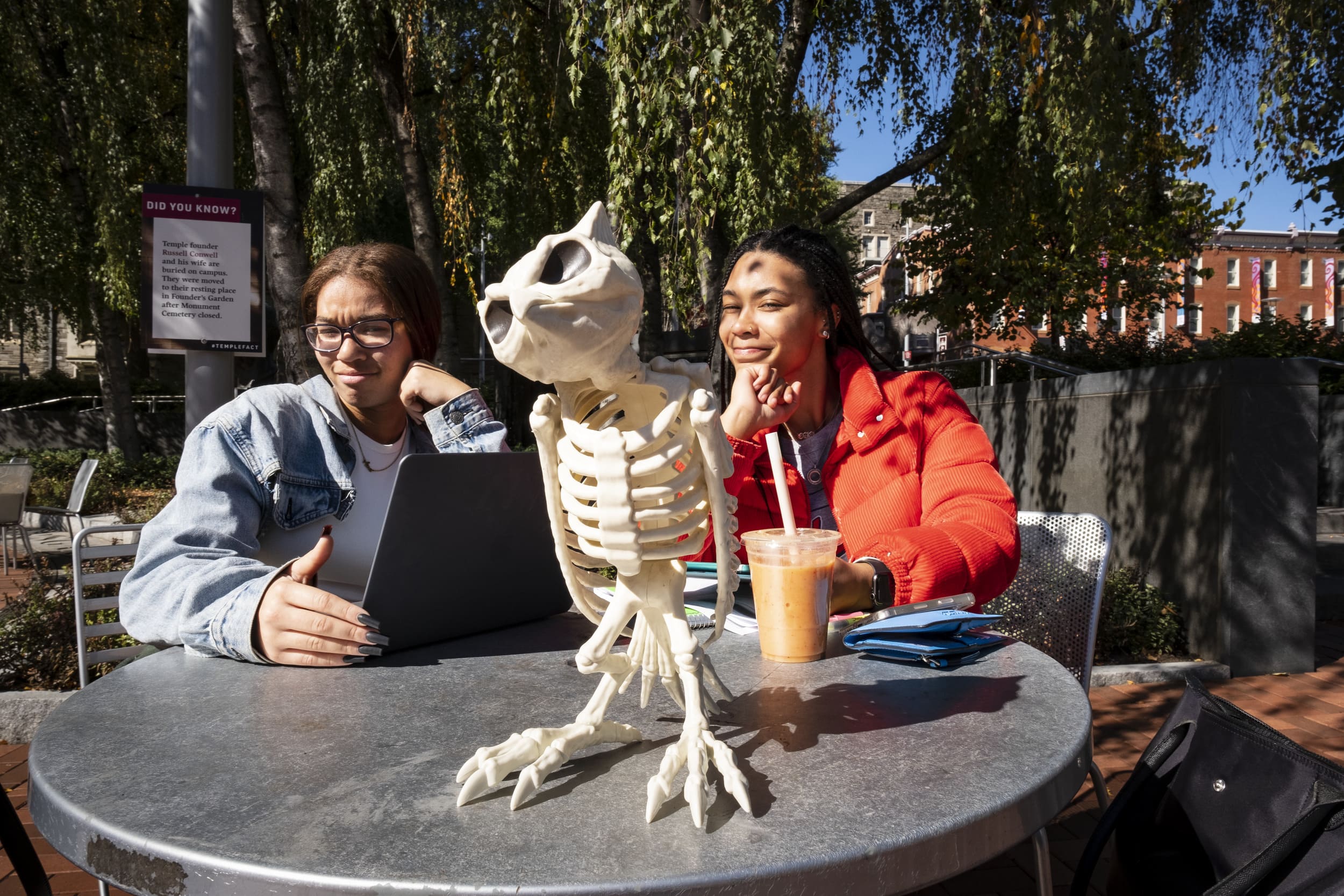Two students sitting at a table outside with a skeleton