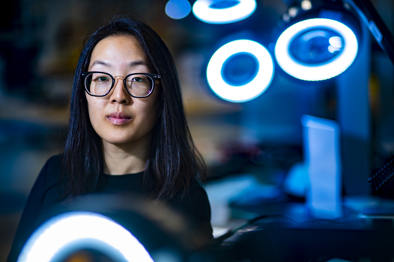 A headshot of Karin Wang. Wang is on the left. There is a blue hue to the photo with several ring lights in the background on the right side.