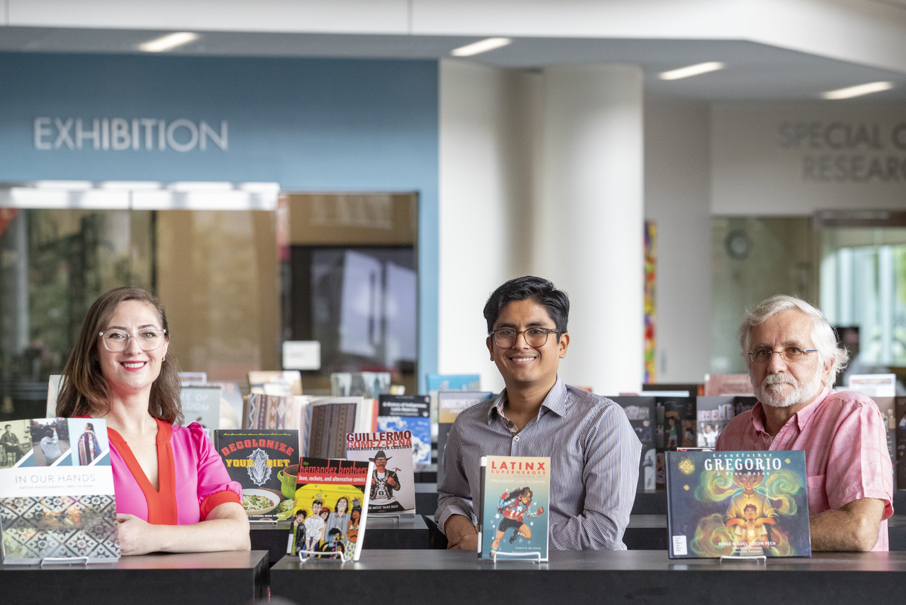 Professors Christina Baker, César Cabezas and Augusto Lorenzino standing in front of books on display in Charles Library for Hispanic Heritage Month