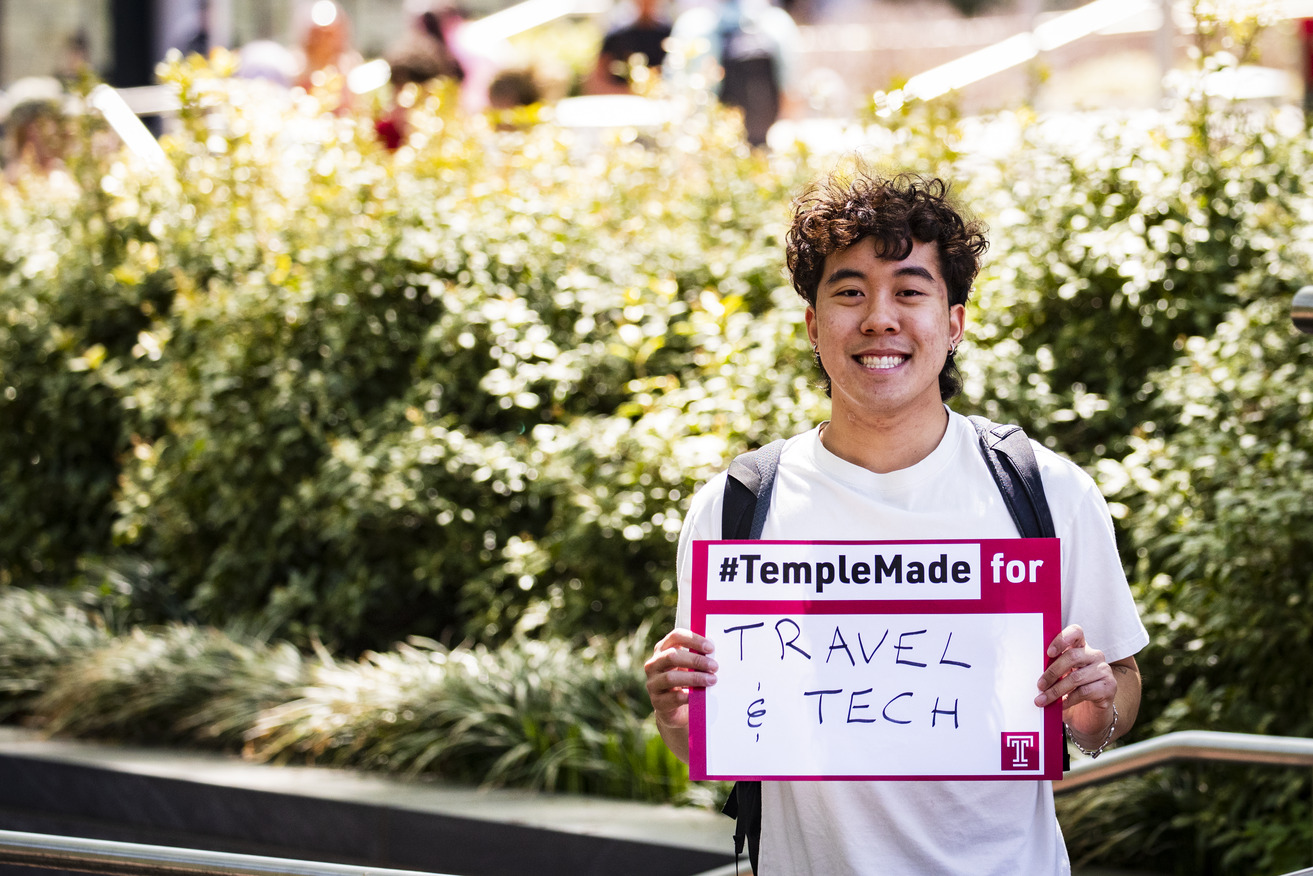 Image of Tran holding a sign that says “#TempleMade for travel and tech”