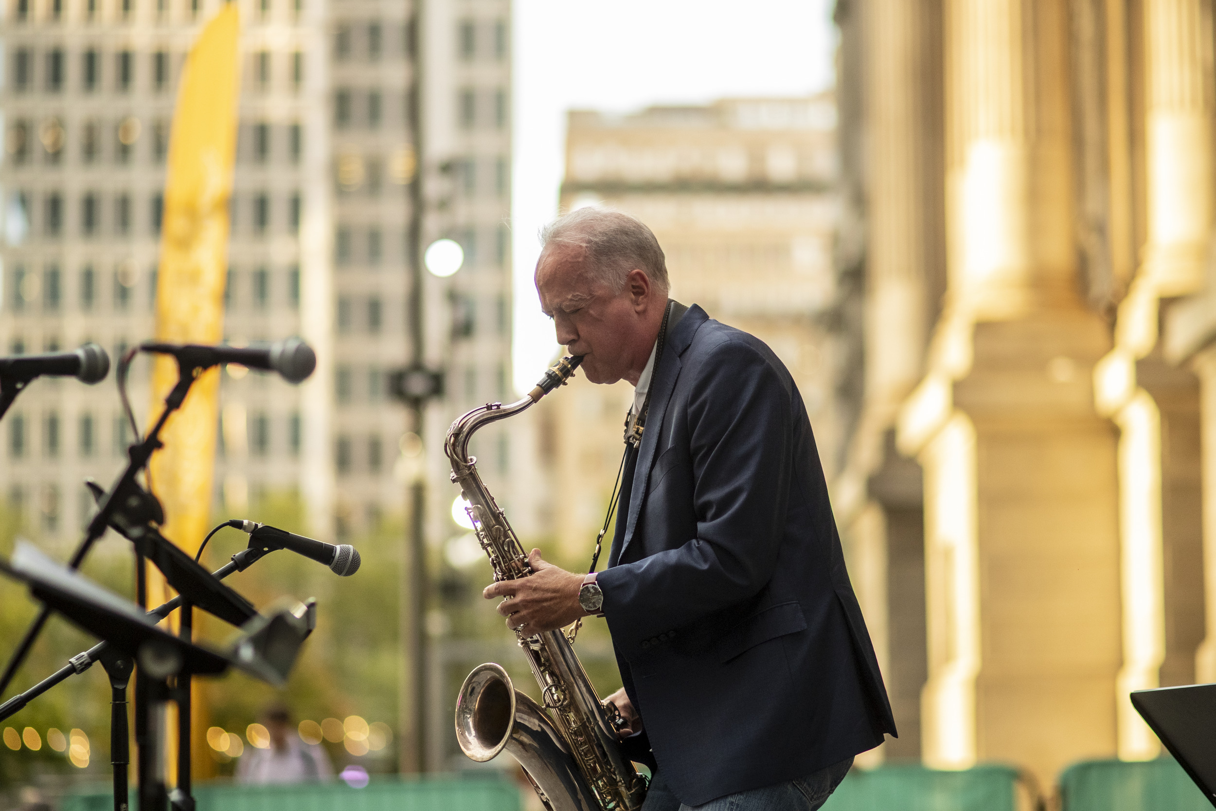 Man with gray hair playing tenor saxophone in a city park