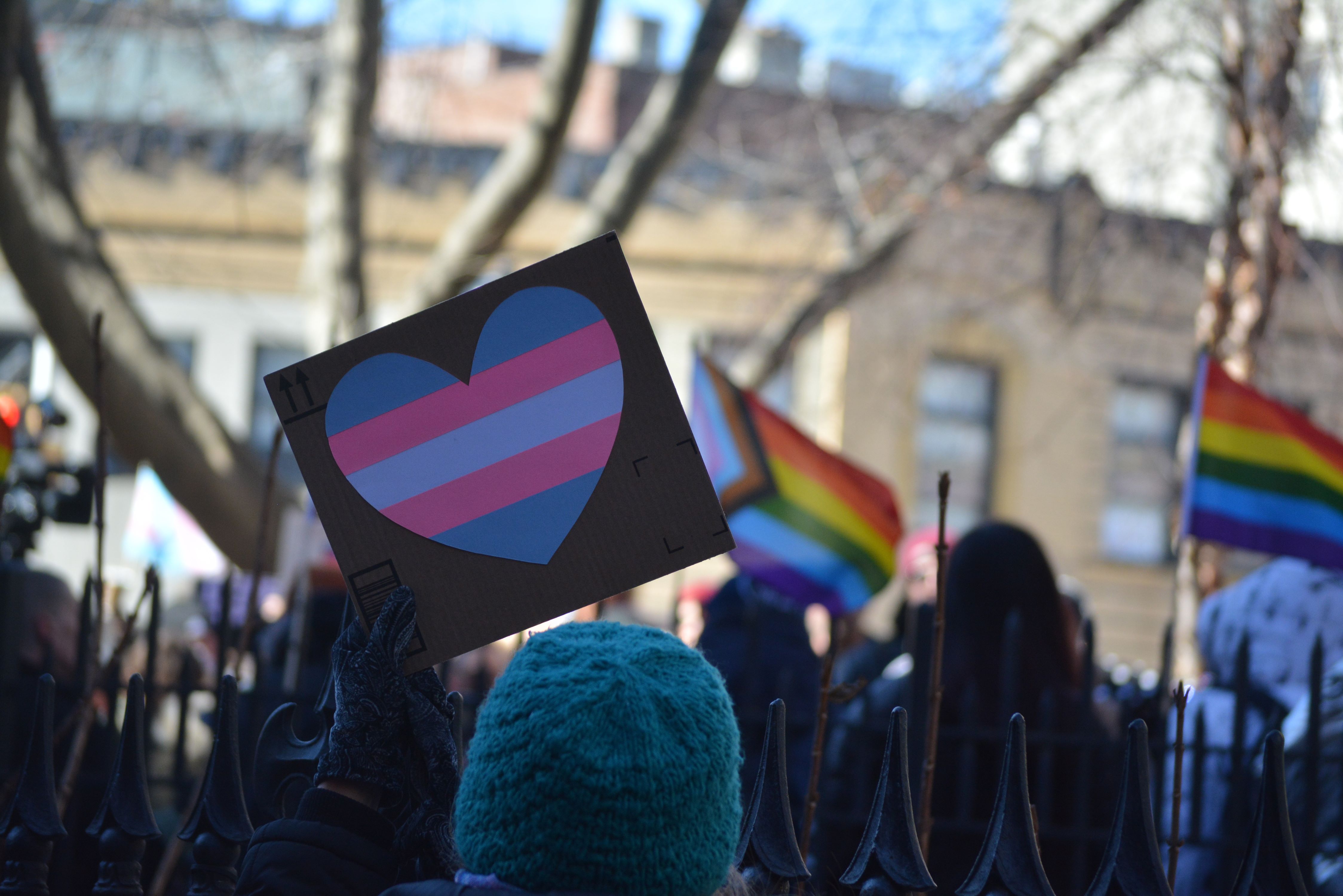 A person holds a black sign with a heart colored in blue, pink and white stripes to acknowledge transgender people.