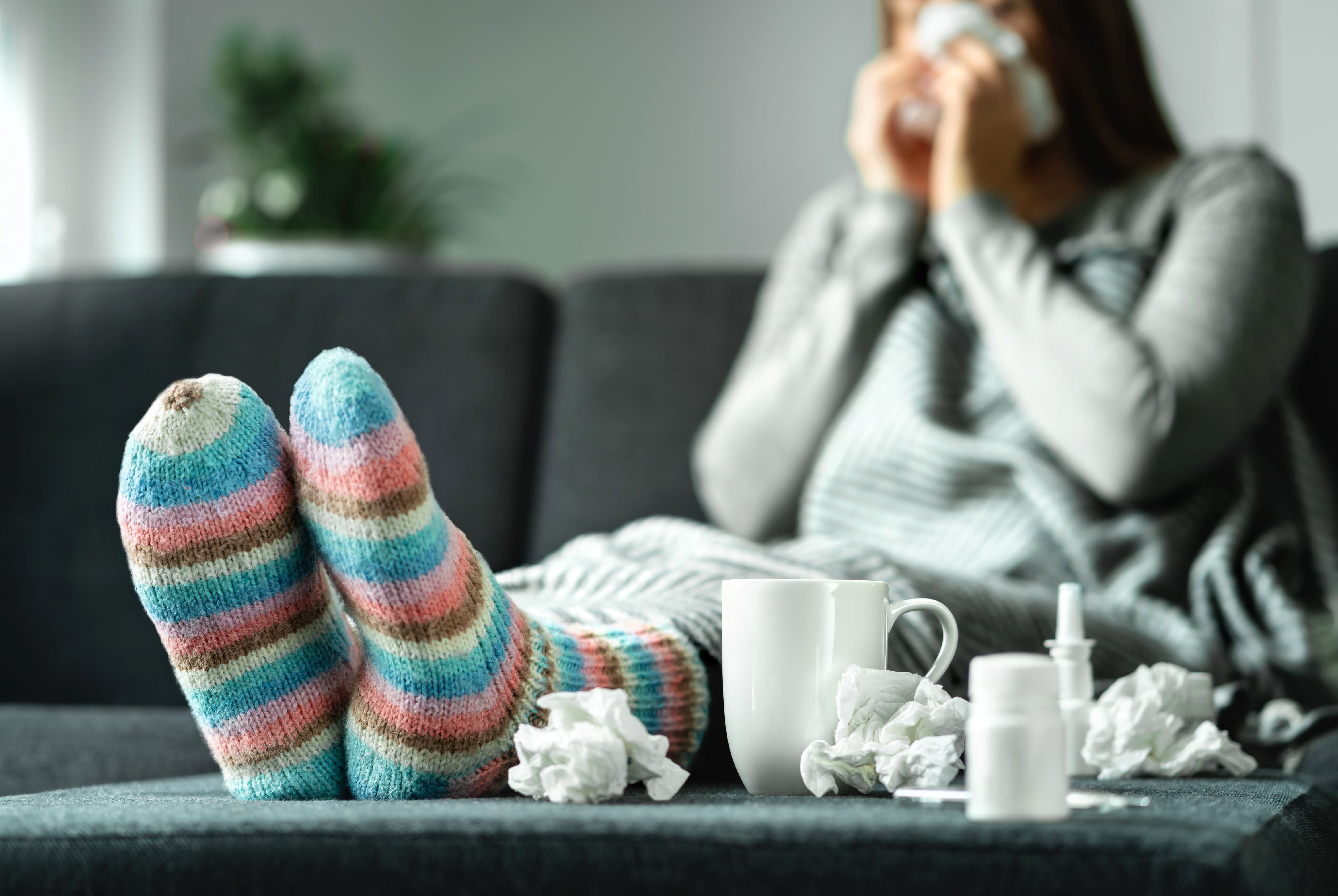 Woman sits on a couch, blowing her nose