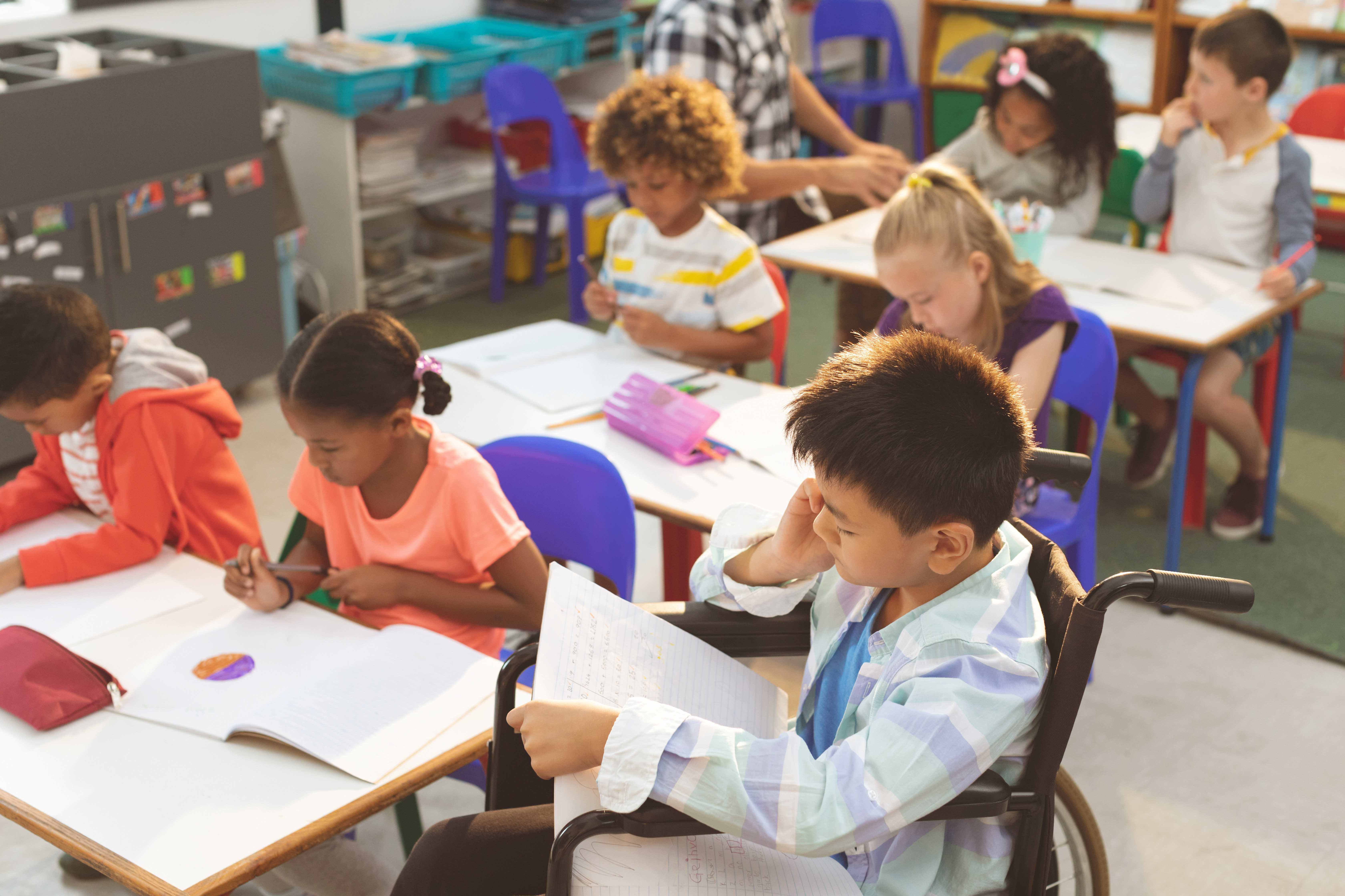 Children sit in a classroom. Young boy in the foreground sits in a wheelchair