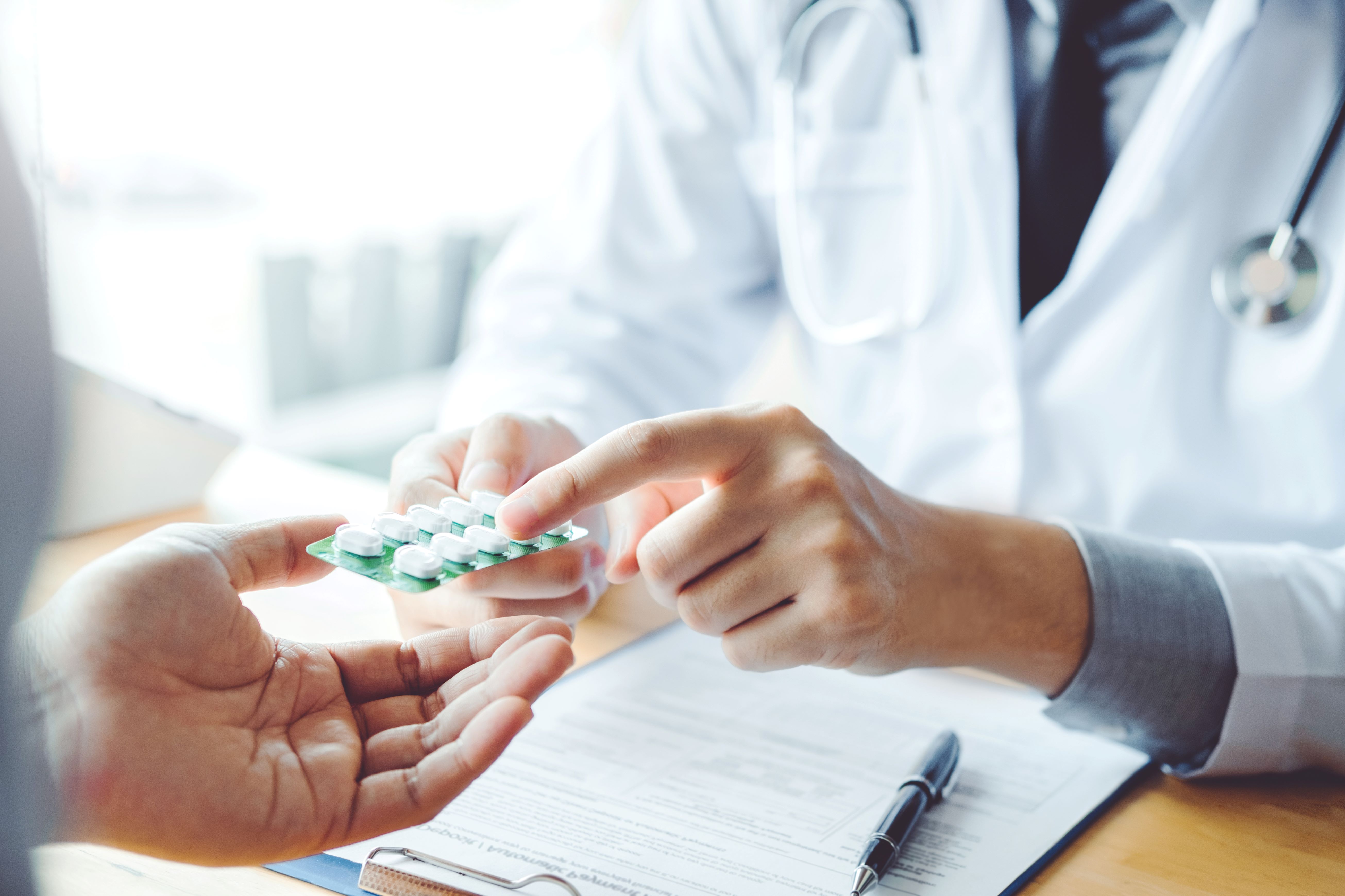 Tight cropped image shows a person in a doctors white coat hands a blister pack of medication to a hand.