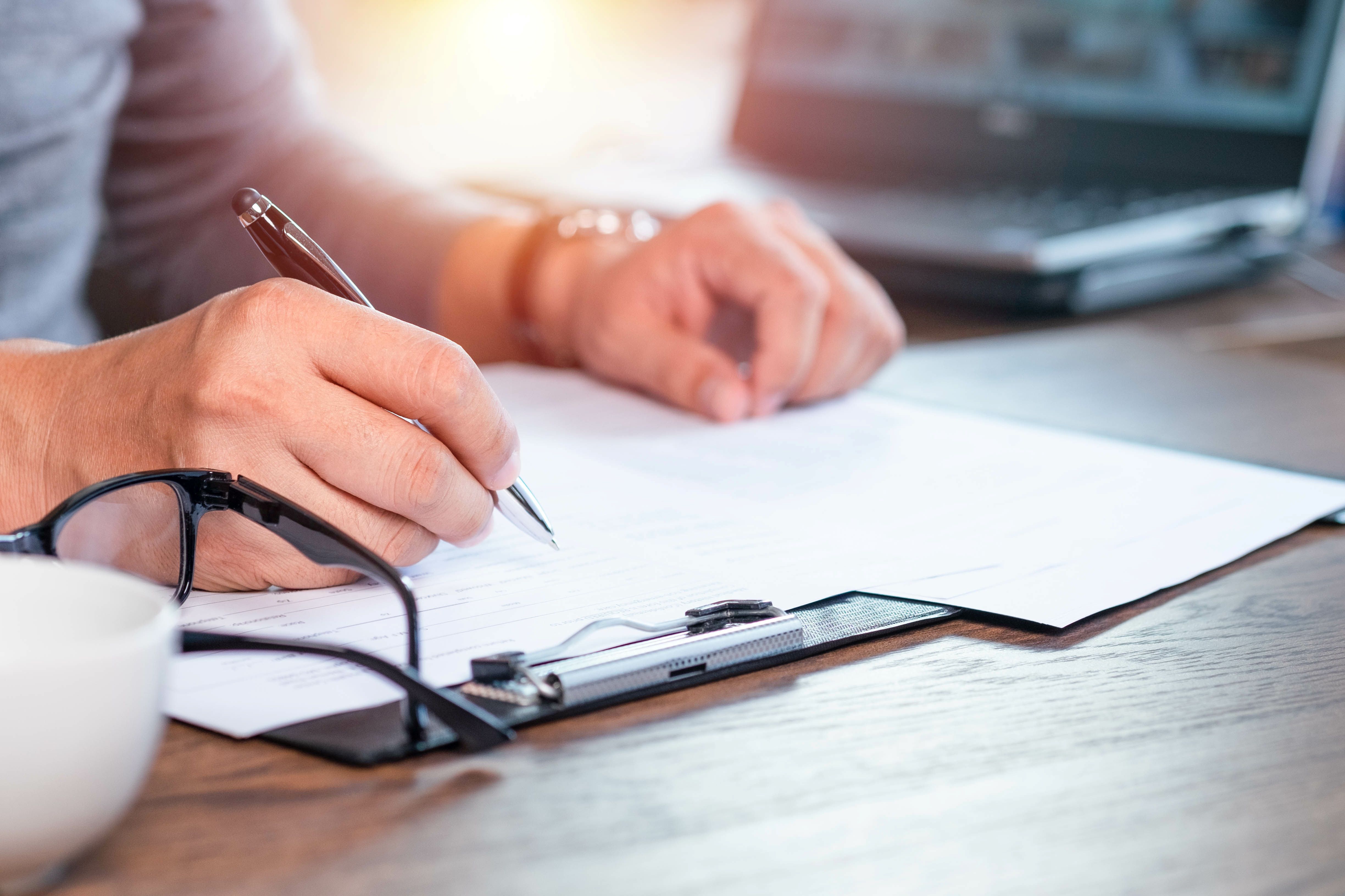 White skinned hands writing on a paper on a clipboard