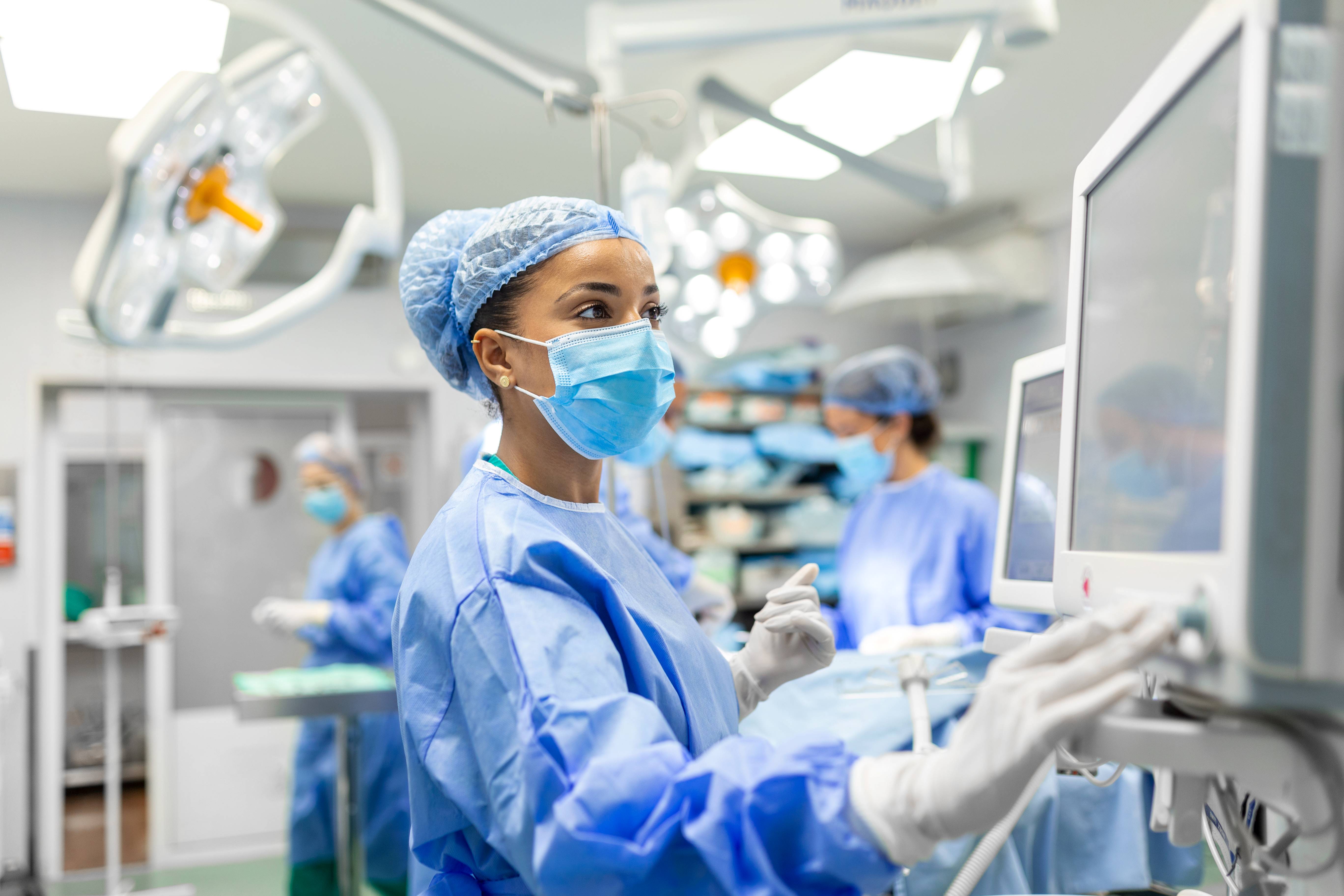 Health care worker in a face mask and hair covering observes a monitor