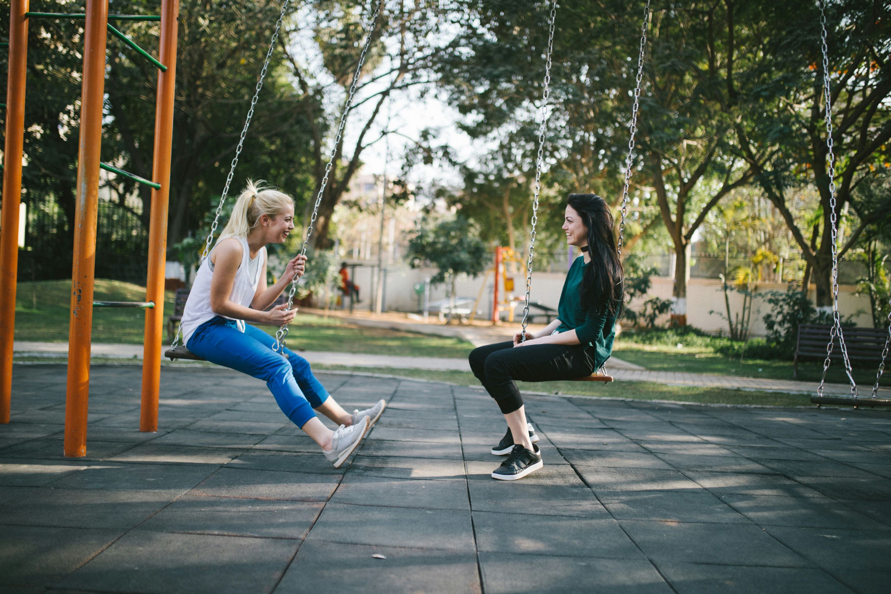 Two women sit opposite each other on a swing set