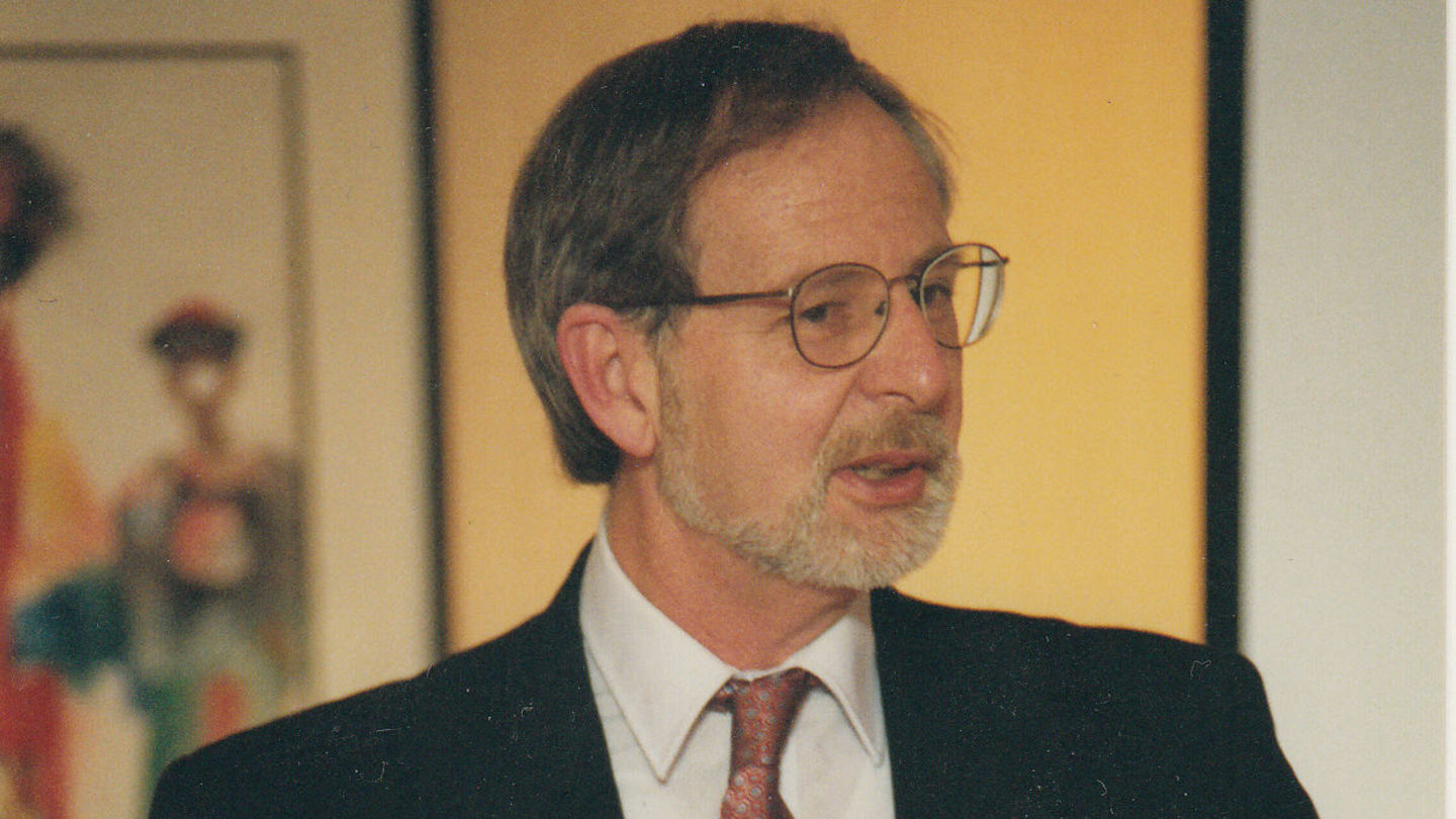 A close up photo of Brian Butz, PhD from several years ago. Butz is wearing a suit jacket and tie with glasses. He is looking off to the side of the camera.