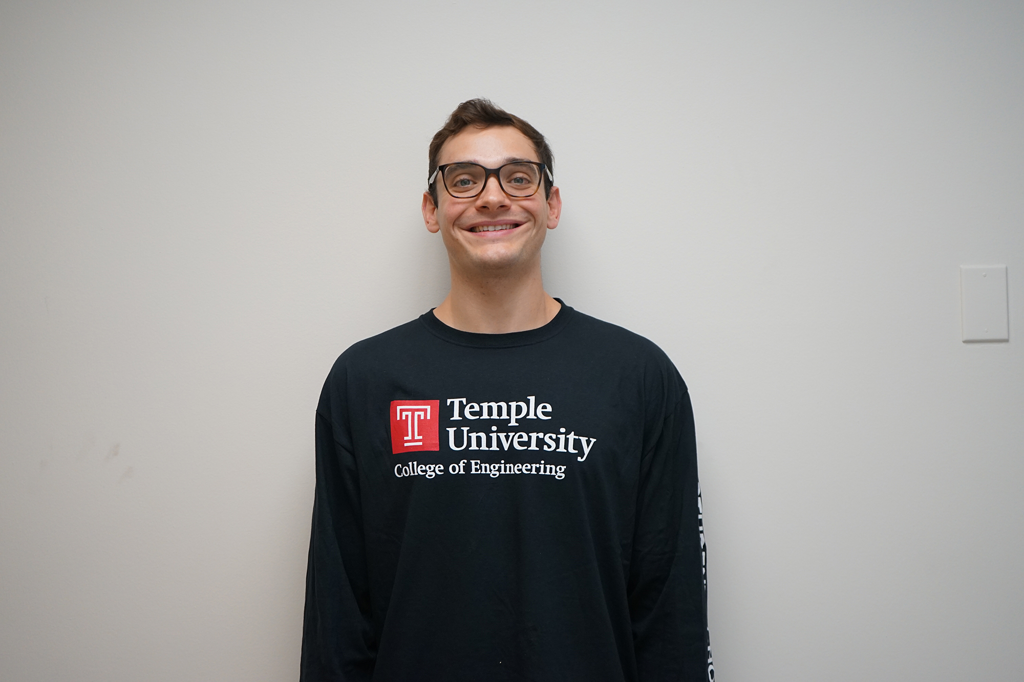 Kyle McGinley standing in front of a white wall. He is wearing a black College of Engineering shirt.