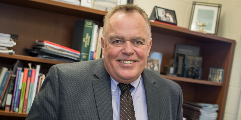 Christopher McGinley sitting in front of a bookshelf. 