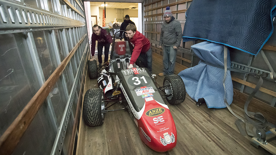 Two students pushing the race car into a truck bed. 