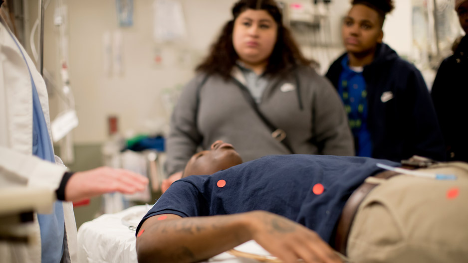 a student lying on a stretcher in a trauma bay as Amy Goldberg teaches.