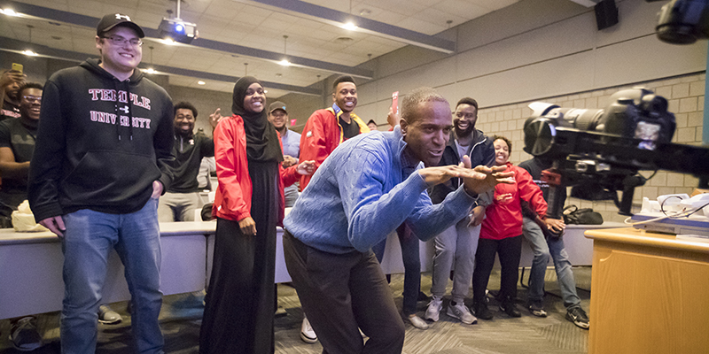 Aaron Smith singing to the camera with his students in the background. 