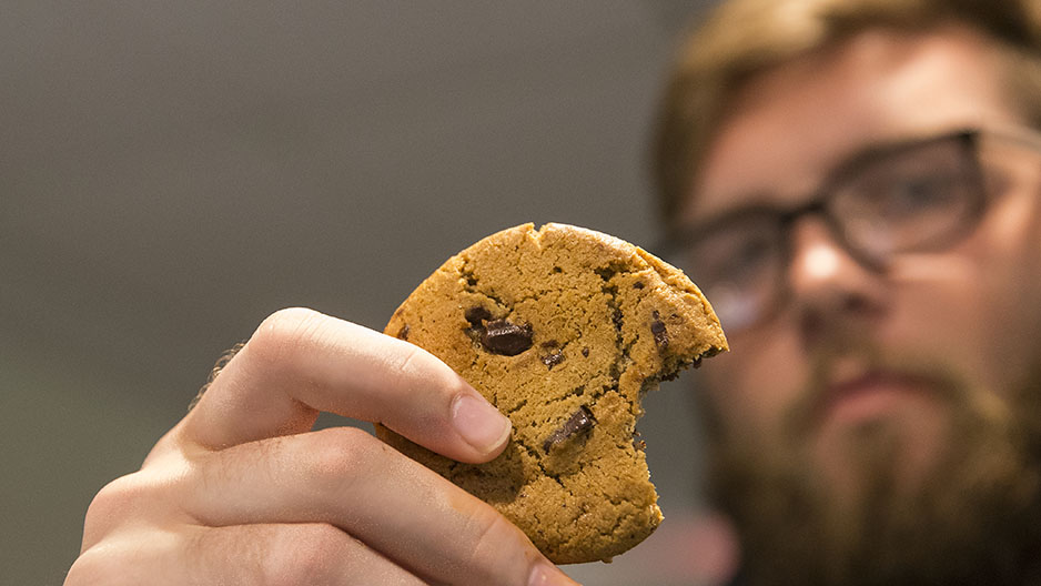 Cole Boozer holding up a cookie with a bite taken out of it. 