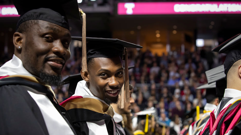 Two male graduates wearing caps and gowns at Commencement