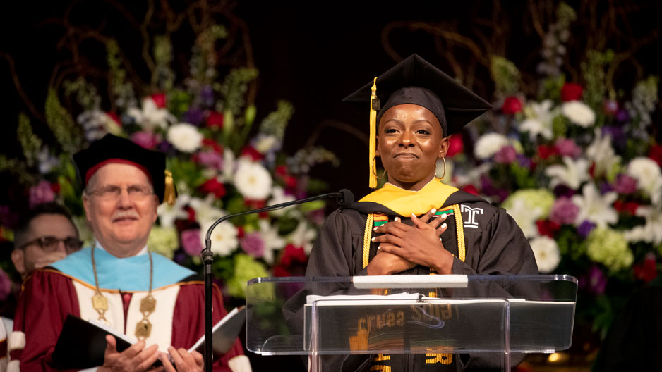 student commencement speaker at a podium with her hands crossed at her chest.