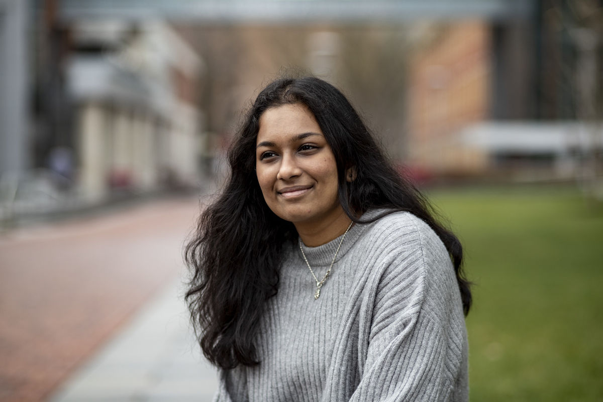 Isha Dev wearing a grey sweater and smiling in on campus.