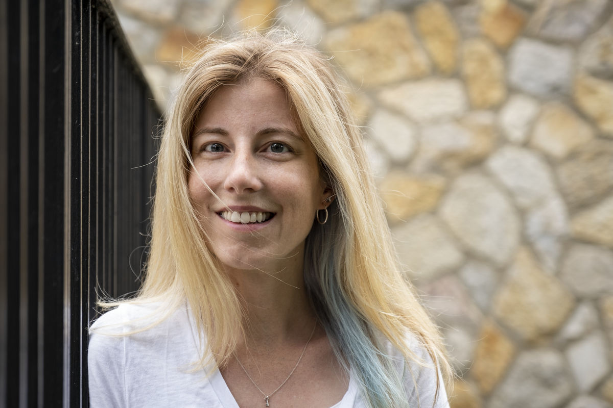 Jennifer Pollitt standing in front of a rock wall, wearing a white t-shirt.