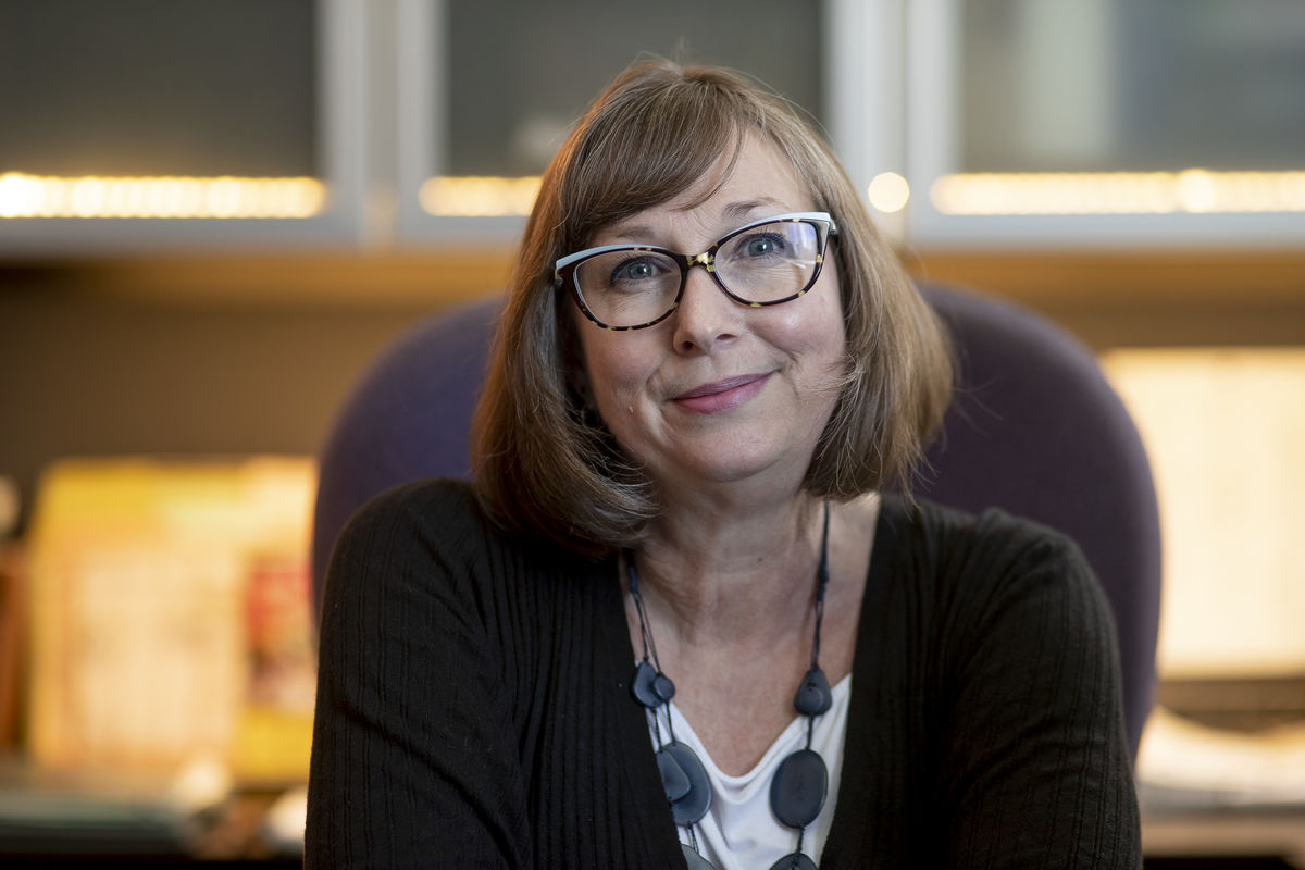 Andrea Vassard sitting at a desk, wearing glasses and smiling.