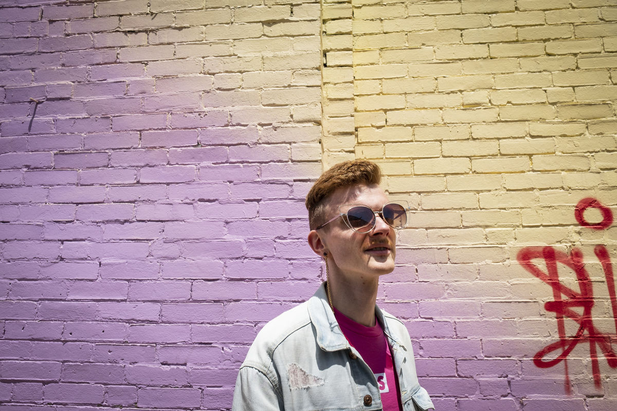 Andreas Copes standing in front of a purple and yellow brick wall, wearing sunglasses.