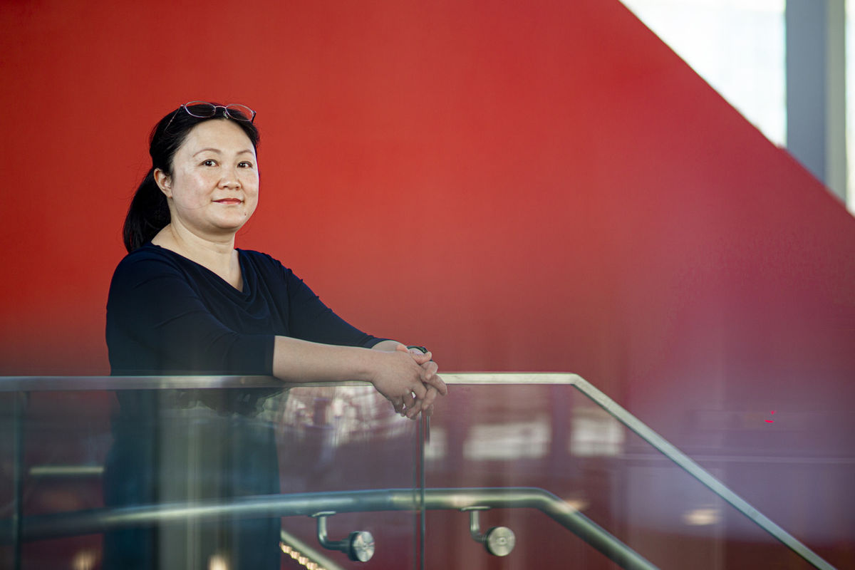 Image of Yun Zhu leaning on a staircase in front of a red background.