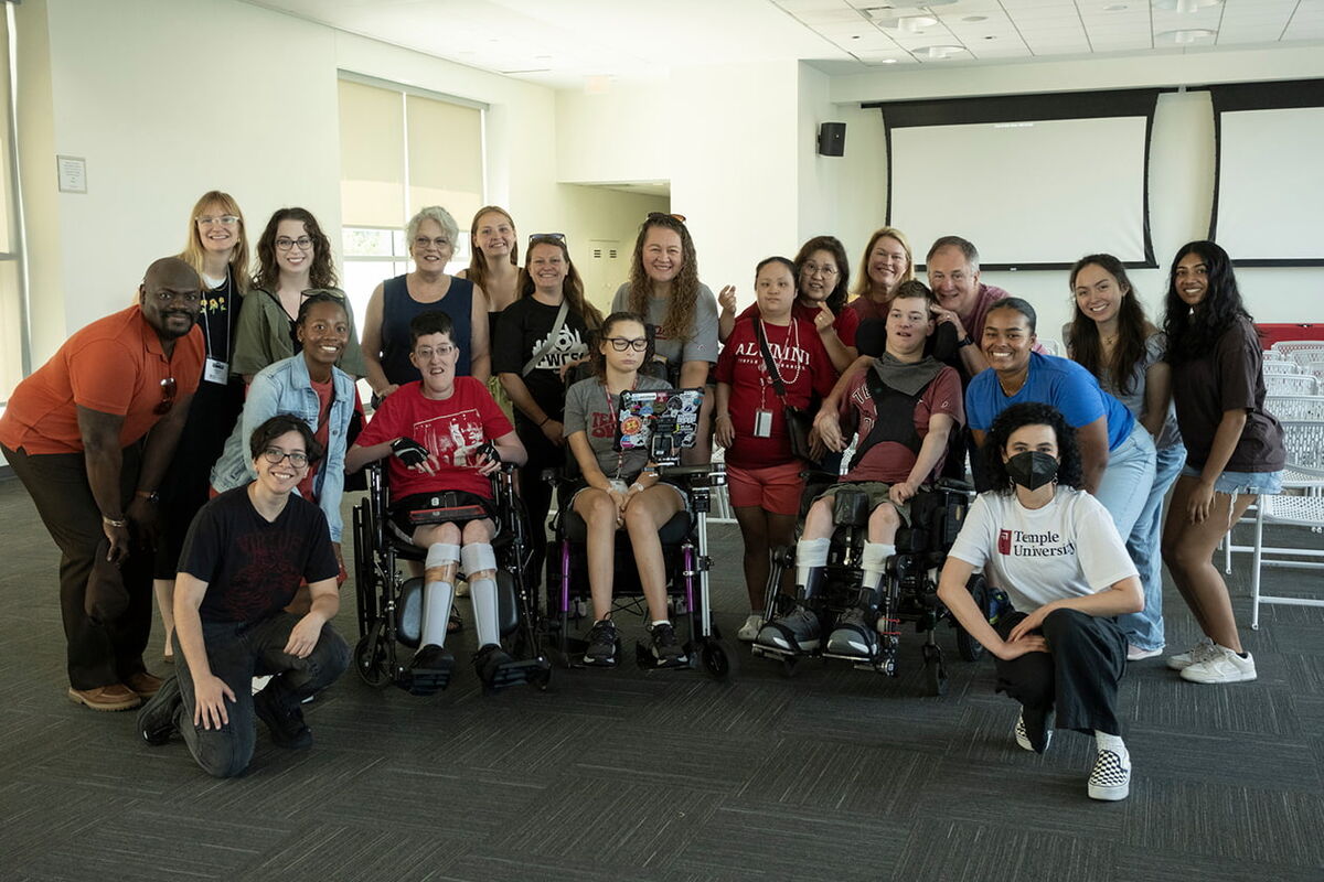 Participants, caregivers, and staff pose in two rows for a photo. Most are smiling and looking at the camera. 