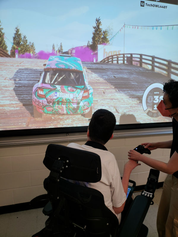 Young adult student with teacher, learning use of adapted controller for xbox