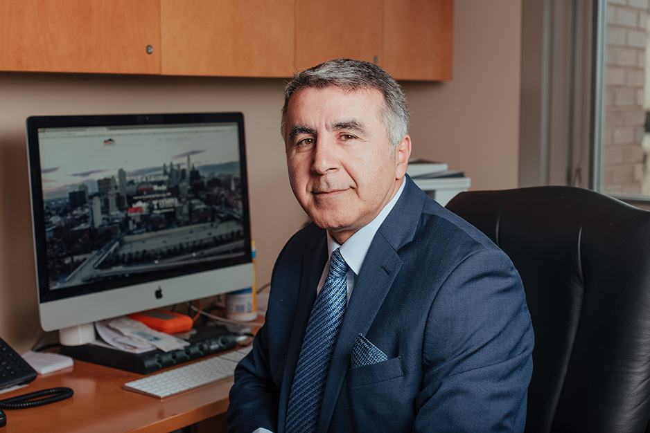 A headshot of Keya Sadeghipour seated at his desk. He is sitting angled towards the camera wearing a suit.