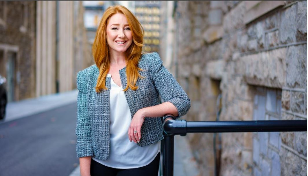 Woman with red hair stands by a building