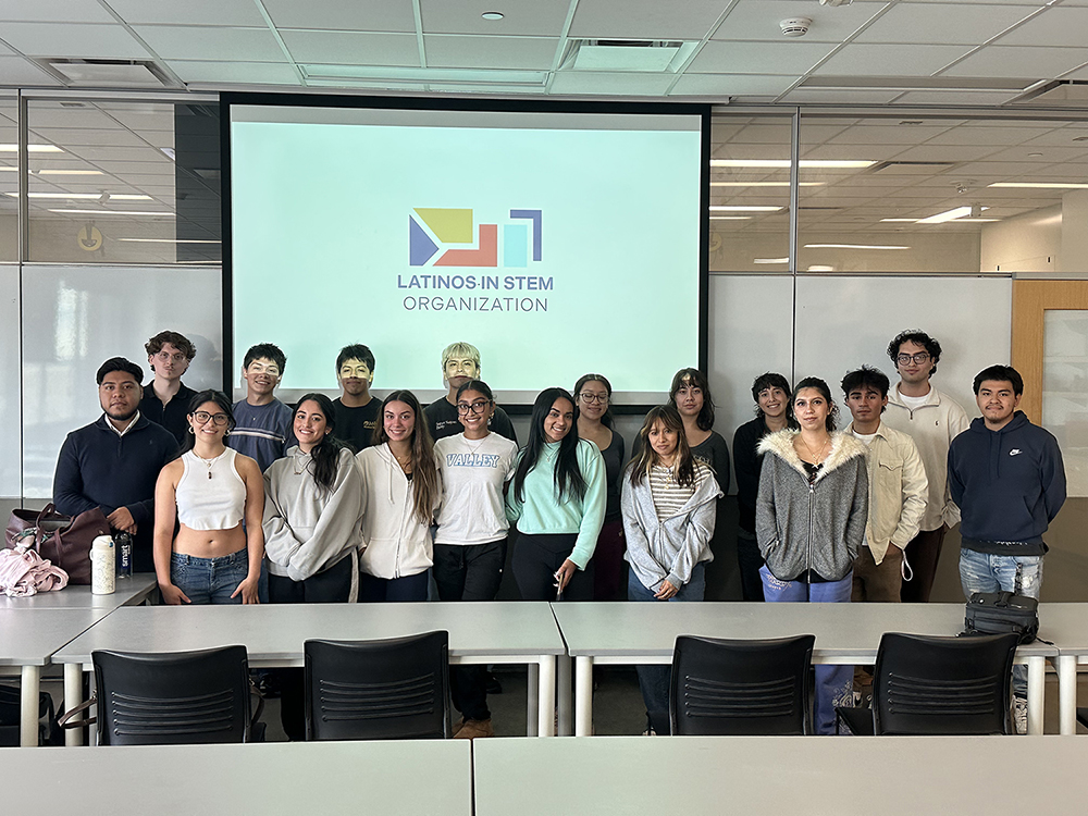 A group photo of LSTO members in a classroom. There are 18 students posing as a group in front of a projector screen with the LSTO logo on it.