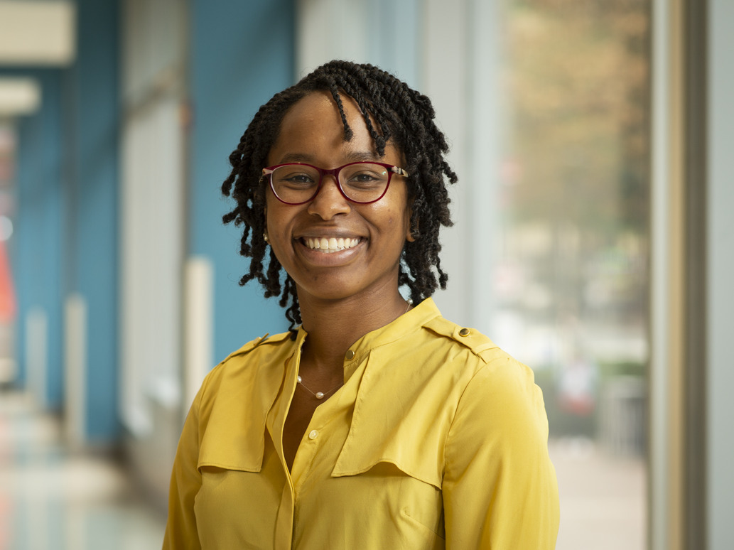 a professor in a yellow shirt standing before a window.