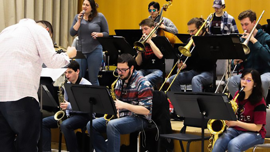 Multiple musicians rehearsing together with a conductor