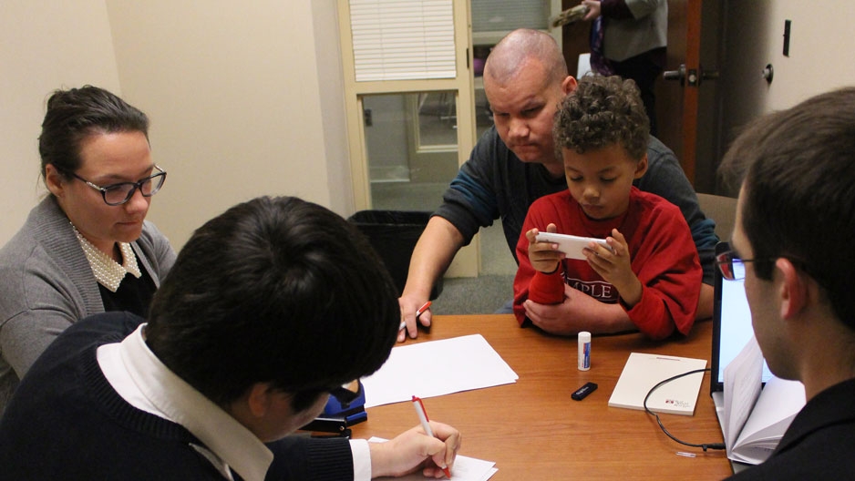 a man looking over forms with attorneys as his young son sits on his lap.