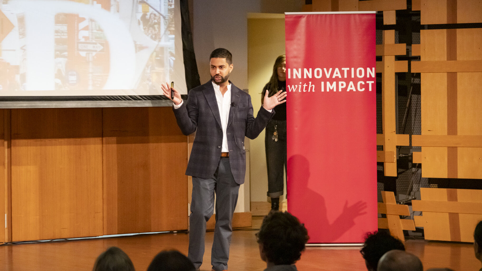 Professor stand on a stage next to Innovation with Impact sign
