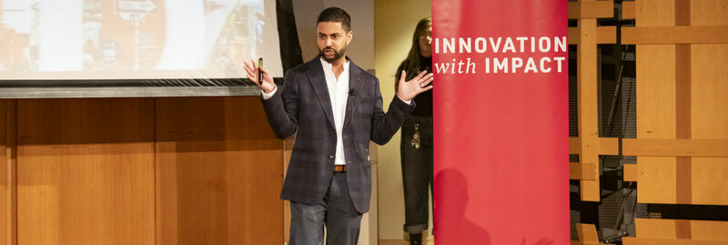 Professor stand on a stage next to Innovation with Impact sign