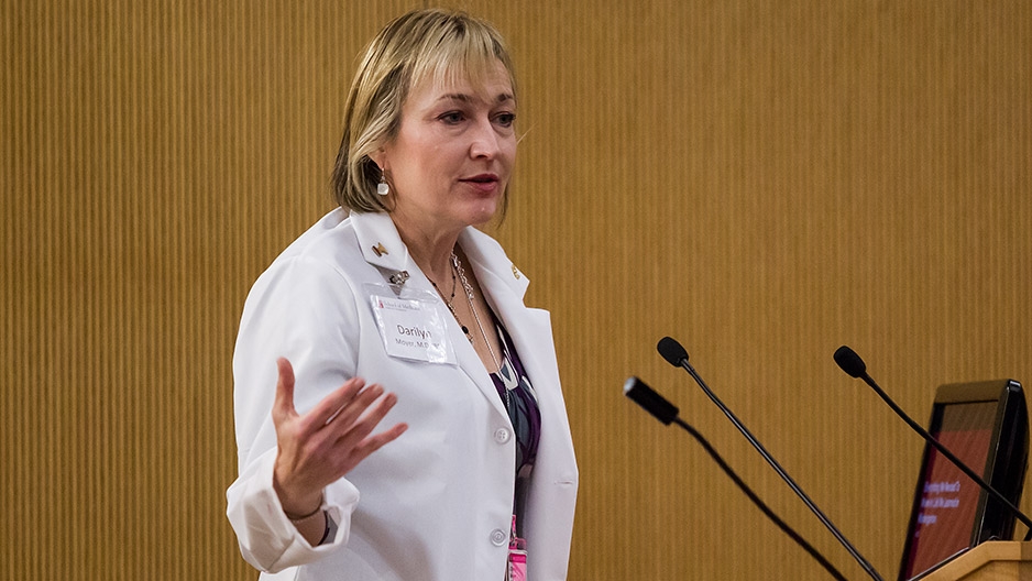 Darilyn Moyer wearing a lab coat and speaking at a podium.