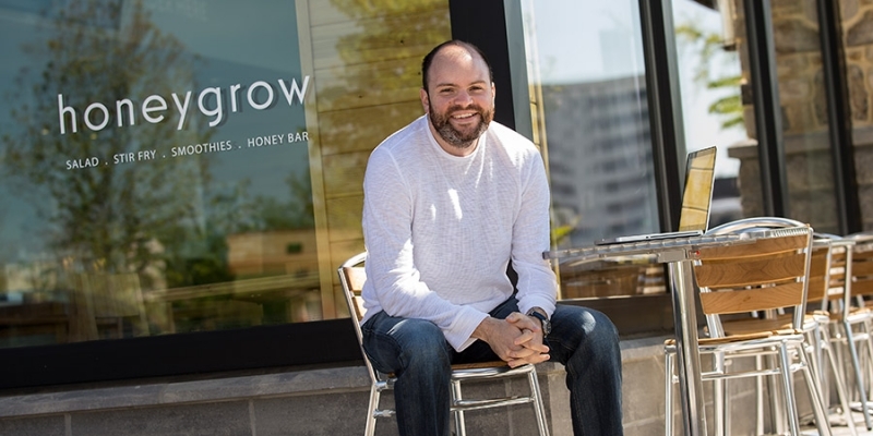 Justin Rosenberg sitting at a table outside of a honeygrow location.